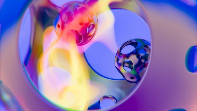 A glossy 3D render of perforated spheres in vivid pink, blue and yellow, reflected inside a translucent curved surface.