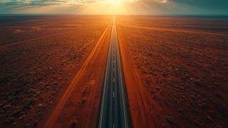 Aerial view of a straight highway running to the horizon across the red Australian outback at golden hour
