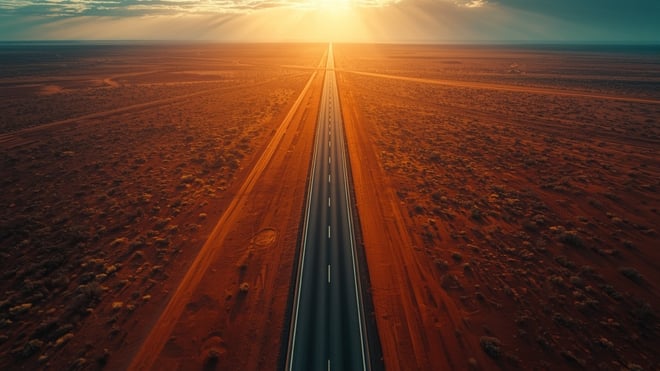 Aerial view of a straight highway running to the horizon across the red Australian outback at golden hour