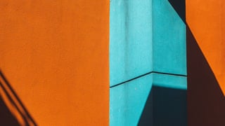 Bold orange and teal building facades meeting at an angle, with strong diagonal shadow.