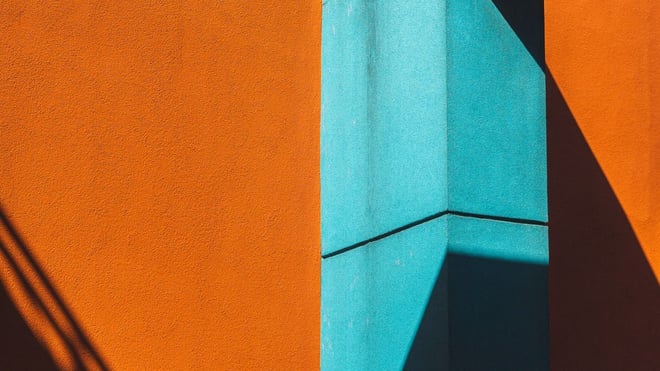 Bold orange and teal building facades meeting at an angle, with strong diagonal shadow.