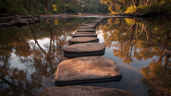 Sandstone stepping stones crossing a still bush creek at golden hour, with eucalyptus trees reflected in the water