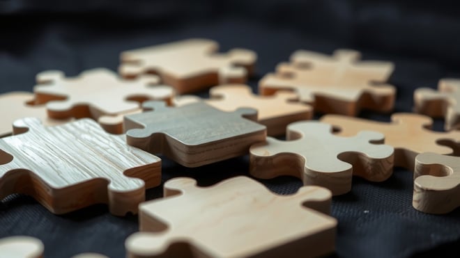 Plain wooden jigsaw puzzle pieces on dark fabric, one piece lifted above the gap